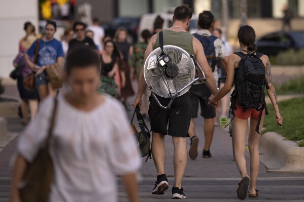 FILE - A girl walks holding hands with a man carrying an electric fan on his back on a hot evening in Bucharest, Romania, July 25, 2023. The rate Earth is warming hit an all-time high in 2023 with 92% of last year’s surprising record-shattering heat caused by humans, top scientists calculated. (AP Photo/Andreea Alexandru, File)