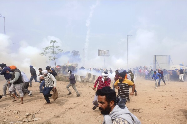 Farmers run for cover after police fired tear gas to disperse protesting farmers who were marching to New Delhi near the Punjab-Haryana border at Shambhu, India, Tuesday, Feb.13, 2024. Farmers are marching to the Indian capital asking for a guaranteed minimum support price for all farm produce. (AP Photo/Rajesh Sachar)