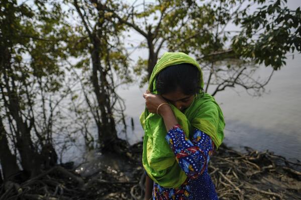 Reshma Begum, 28, wipes her tears as she stands on her lost land, narrating how Cyclone Amphan destroyed her house at South Kainmari, in Mongla, Bangladesh, March 4, 2022. Begum used to catch fish in the river that swallowed her home, making her three-member family homeless. Now she lives temporarily on another man’s land and works at a factory in the export processing zone. (AP Photo/Mahmud Hossain Opu)