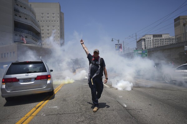 EDS NOTE: OBSCENITY - A protester gestures as tear gas is used near the Metropolitan Detention Center in downtown Los Angeles, Sunday, June 8, 2025, following last night's immigration raid protest. (AP Photo/Eric Thayer)