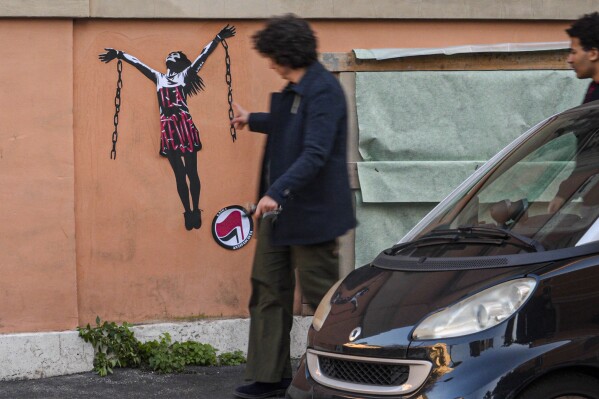 Passersby look at a mural painting depicting Italian antifascist activist Ilaria Salis in the act of breaking her chains near the Hungarian Embassy in Rome, Wednesday, Jan. 31, 2024. Italy has ramped up its protests over the treatment of Salis being held in a Hungarian jail after images of her appearing chained and shackled at a Budapest court hearing this week sparked outrage here. (AP Photo/Luigi Navarra)
