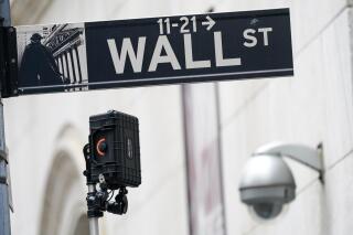 FILE - A Wall Street sign is seen next to surveillance equipment outside the New York Stock Exchange, Oct. 5, 2021, in New York. Stocks are falling in early trading Monday, Dec. 20, 2021 continuing a weak stretch as traders keep a wary eye on global increases in COVID-19 cases. Traders also got news over the weekend that a key U.S. senator wouldn't support President Joe Biden's $2 trillion domestic spending bill, putting its passage in doubt. (AP Photo/Mary Altaffer, file)