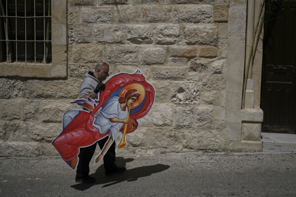 A man carries a large cutout of an angel outside the Maronite Church of St. George during preparations for the Washing of the Feet ceremony in Quraye, near the southern port city of Sidon, Lebanon, Thursday, April 17, 2025. (AP Photo/Hassan Ammar)