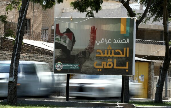In this Tuesday, July 2, 2019 photo, motorists pass by a Popular Mobilization poster in Baghdad, Iraq. The Iraqi government's move to place Iranian-backed militias under the command of the armed forces is a political gamble by a prime minister increasingly caught in the middle of a dangerous rivalry between Iran and the U.S., the two main power brokers in Iraq. Facing pressure from the U.S. to curb the militias, the move allows Prime Minister Adel Abdul-Mahdi to portray a tough stance ahead of a planned visit to Washington. It is unlikely, though, that he would be able to rein in and neutralize Iran-supported groups and he risks coming off as a weak and ineffective leader if he doesn't. The Arabic sentence on the poster reads, "the Popular Mobilization is Iraqi and will last." (AP Photo/Hadi Mizban)