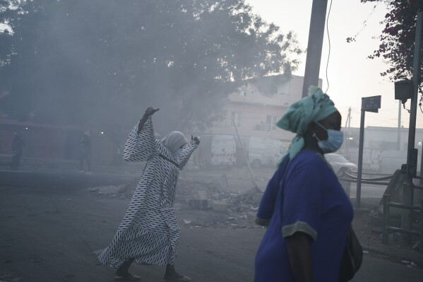 Women cross a street filled with smoke during clashes between demonstrators and police in Dakar, Senegal, Saturday, June 3, 2023. (AP Photo/Leo Correa)