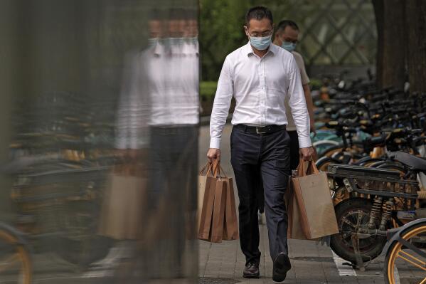 A man wearing a face mask to help protect from the coronavirus carries goody bags as he walks by a row of bicycles parked along a pavement in Beijing, Monday, Sept 13, 2021. (AP Photo/Andy Wong)