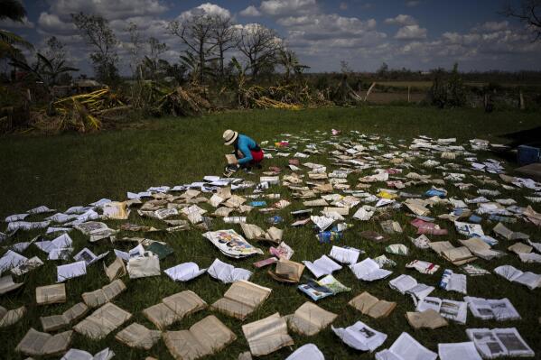 A teacher dries out books at a school that was heavily damaged by Hurricane Ian in La Coloma, in the province of Pinar del Rio, Cuba, Wednesday, Oct. 5, 2022. (AP Photo/Ramon Espinosa)