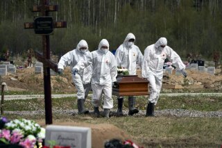 ARCHIVO - En esta magen de archivo del 15 de mayo de 2020, enterradores con trajes de protección llevan el ataúd de una víctima de COVID-19, mientras familiares y amigos guardan las distancia en una zona del cementerio reservada a víctimas del virus, en Kolpino, a las afueras de San Petersburgo, Rusia. (AP Foto/Dmitri Lovetsky, Archivo)