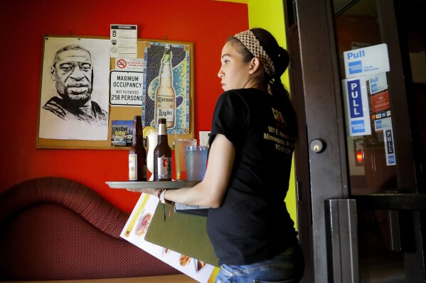 Princis Mercedes carries drinks for customers near a portrait of her former coworker, George Floyd, in the lobby of Conga Latin Bistro in Minneapolis on June 7, 2020. (AP Photo/Julio Cortez, File)
