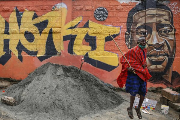 FILE - In this Wednesday, June 3, 2020 file photo a Maasai man, who said he had seen videos on Facebook about protests in the U.S. over the death of George Floyd, jumps next to a new mural painted this week showing Floyd with the Swahili word "Haki" meaning "Justice", in the Kibera slum, or informal settlement, of Nairobi, Kenya. Since George Floyd's death in the U.S. state of Minnesota last week, his face has been painted on walls from Nairobi, Kenya to Idlib, Syria. Floyd's name has been inked on the shirts of soccer players and chanted by crowds from London and Cape Town to Tel Aviv and Sydney. (AP Photo/Brian Inganga, File)