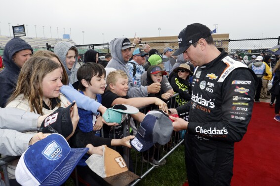 Driver Kyle Busch, right, gives autographs before a NASCAR Cup Series auto race at Kansas Speedway in Kansas City, Kan., Sunday, May 5, 2024. (AP Photo/Colin E. Braley)
