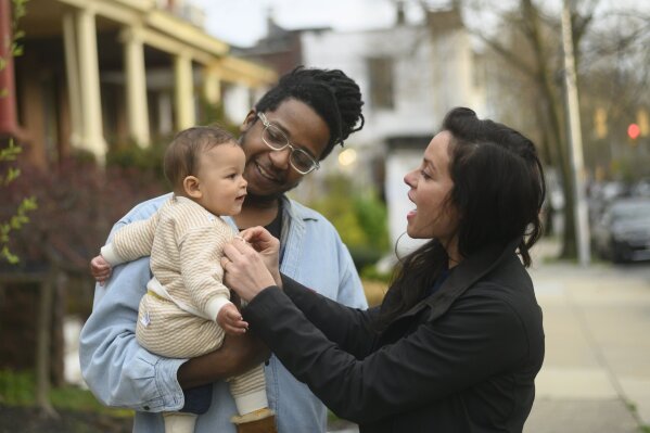 Nurse practitioner Katharine Billipp, 38, stands with her husband, Jay Lawson, and daughter, Genevieve, outside their home in Baltimore, Md., on Friday, April 3, 2020. Billipp, who works with patients who are poor, very sick and staying in shelters, encampments or abandoned buildings amid the COVID-19 coronavirus outbreak, says, “We find ourselves on the front lines, without proper equipment, being the potential vector of disease to our underserved and most at-risk patients.” (AP Photo/Juliet Linderman)