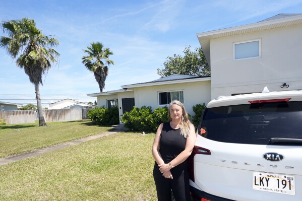Amy Chadwick poses outside her current home Monday, April 8, 2024, in Satellite Beach, Fla. Chadwick, a victim of the fires in Hawaii, moved to Florida where she could stretch her homeowners insurance dollars while she waits for her lot to be cleared and for permission to rebuild. (AP Photo/John Raoux)
