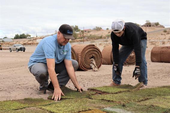 Matt Hanrahan, left, chairman of the Boys & Girls Clubs of the Colorado River board, and volunteer Evan Oehler lay pieces of the Guaranteed Rate Bowl field into place in December 2021 at the site of the new Fort Mohave, Ariz., Boys & Girls Club facility. (Chris Higa/Mohave Valley Daily News via AP)