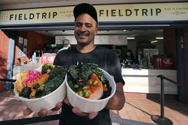 FILE - This Aug. 30, 2019 photo shows chef JJ Johnson posing with two signature rice bowls, one salmon and one vegetable, outside his Field Trip counter-service restaurant kiosk on the food court at the US Open tennis championships in New York. Johnson's new cookbook "The Simple Art of Rice: Recipes from Around the World for the Heart of Your Table," a book co-authored with Danica Novgorodoff, celebrates rice's versatility. (AP Photo/Charles Krupa, File)