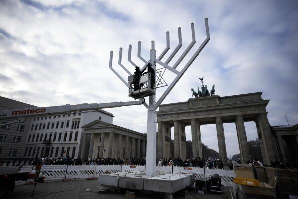 Rabbi Yehuda Teichtal, on the platform left, and Rabbi Segal Shmoel, on the platform right, inspect a giant Hanukkah Menorah, set up by the Jewish Chabad Educational Center ahead of the Jewish Hanukkah holiday, in front of the Brandenburg Gate at the Pariser Platz in central Berlin, Germany, Friday, Dec. 16, 2022. Holocaust survivors from around the world are marking the third day of Hanukkah in a virtual ceremony online as Jews are worrying about a sharp increase in antisemitism in the U.S., Europe and elsewhere. (AP Photo/Markus Schreiber)