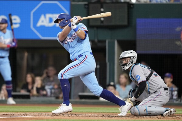 Texas Rangers' Josh Jung, front left, follows through on a swing as Miami Marlins catcher Jacob Stallings, right, looks on in the second inning of a baseball game, Sunday, Aug. 6, 2023, in Arlington, Texas. Jung reached first on a fielder's choice. (AP Photo/Tony Gutierrez)