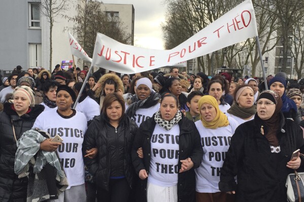 FILE - People march in the streets of Aulnay-sous-Bois, north of Paris, France, holding a sign reading "Justice for Theo" during a protest, a day after a French police officer was charged with with violence during an identity check, Monday, Feb. 6, 2017. A French court convicted three police officers of “voluntary violence” towards a youth worker in a Paris suburb who had a police baton forcibly inserted into his rectum during an identity check seven years ago. (AP Photo/Milos Krivokapic, File)