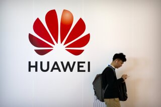 FILE - In this Oct. 31, 2019, file photo, a man uses his smartphone as he stands near a billboard for Chinese technology firm Huawei at the PT Expo in Beijing. The Justice Department has added new ...