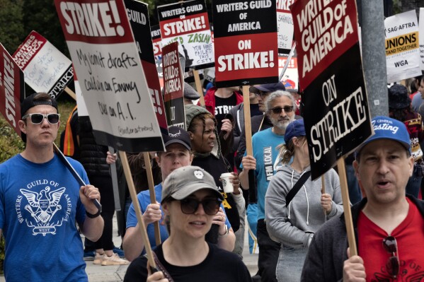 FILE -Picketers pass near a studio entrance during a Writers Guild rally outside Warner Bros. Studios, Wednesday, May 24, 2023, in Burbank, Calif. As a strike drags on, about 1,000 Hollywood writers and their supporters have marched and rallied in Los Angeles for a new contract with studios that includes the payment guarantees and job security they say they deserve. Speakers at Wednesday's event on June 21, emphasized the solidarity the Writers Guild of America has received from other unions. (AP Photo/Richard Vogel, File)