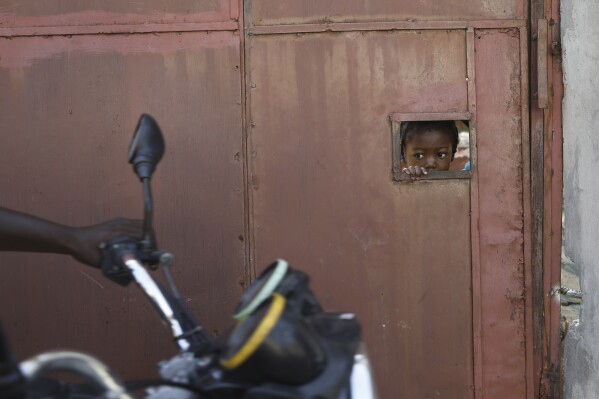 FILE - A child watches from an opening in a security gate as residents flee their homes due to gang violence, in Port-au-Prince, Haiti, March 9, 2024. (AP Photo/Odelyn Joseph, File)