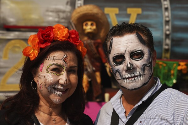 Visitors with faces painted as catrinas pose for photos at Mexico City´s main square the Zocalo, ahead of the Day of the Dead celebrations, Tuesday, Oct. 31, 2023. (AP Photo/Marco Ugarte)