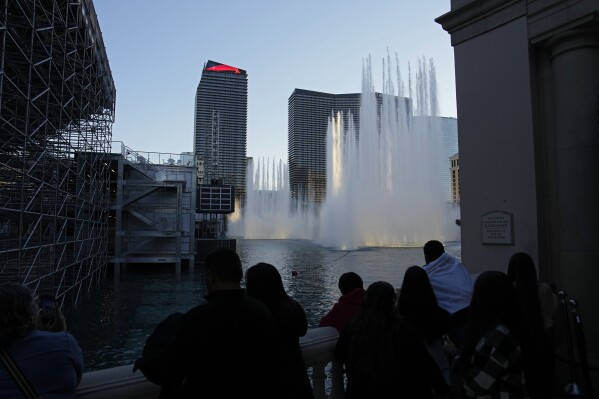 People watch the fountains at the Bellagio hotel-casino behind grandstands installed ahead of the Las Vegas Formula One Grand Prix auto race Friday, Nov. 10, 2023, in Las Vegas. (AP Photo/John Locher)