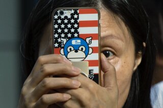 FILE - In this July 26, 2020, file photo, a woman takes a photo with a phone that has a United States flag themed cover outside the United States Consulate in Chengdu in southwest China's Sichuan province. China is delaying the renewal of press cards for at least five journalists working at four U.S. media outlets, an organization of foreign correspondents said Monday, Sept. 7, 2020 making them vulnerable to expulsion in apparent retribution for Washington's targeting of Chinese reporters working in the United States. (AP Photo/Ng Han Guan, File)