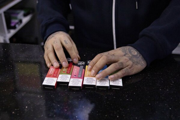 In this Jan. 31, 2020 photo, a vape shop manager shows Puff Bar flavored disposable vape devices at a store in the Brooklyn borough of New York. On Thursday, Feb. 6, 2020, the U.S. government began enforcing restrictions on flavored electronic cigarettes aimed at curbing underage vaping. But parents, researchers and students warn that some young people have already moved on to a newer kind of vape that isn't covered by the flavor ban - disposables. (AP Photo/Marshall Ritzel)