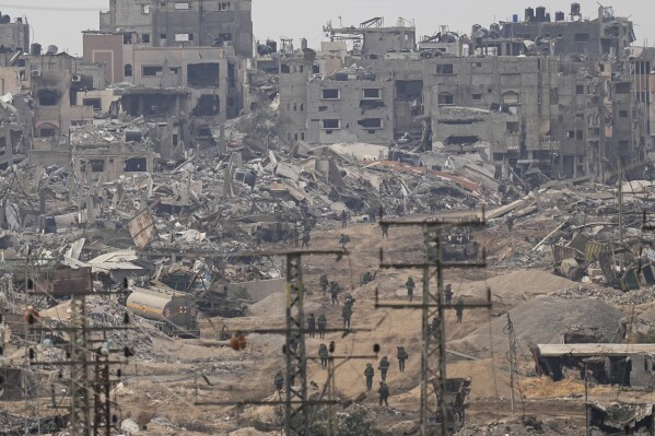Israeli troops walk in the Gaza Strip as seen from southern Israel, Thursday, Dec. 21, 2023. AP Photo/Ohad Zwigenberg)