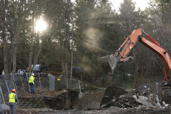 Sunlight breaks through trees as heavy equipment works to demolish the final pieces of the foundation of the house where four University of Idaho students were killed in 2022 on Thursday, Dec. 28, 2023, in Moscow, Idaho. Students Ethan Chapin, Xana Kernodle, Madison Mogen and Kaylee Goncalves were fatally stabbed there in November 2022. (AP Photo/Ted S. Warren)