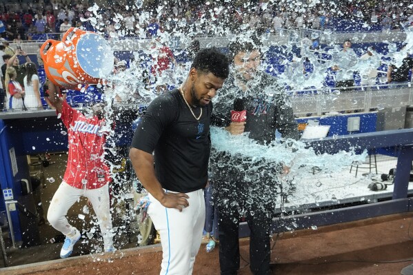 Miami Marlins second baseman Otto Lopez, center, is doused by Jazz Chisholm Jr., left rear, as Lopez does an interview after a baseball game against the New York Mets, Saturday, May 18, 2024, in Miami. Lopez hit a single to score Christian Bethancourt to beat the Mets 10-9 in 10 innings. (AP Photo/Wilfredo Lee)