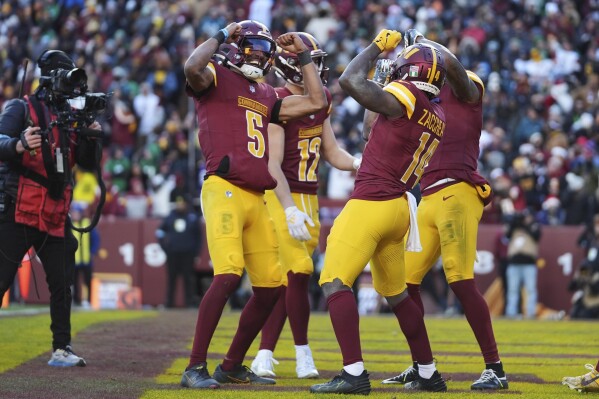 Washington Commanders wide receiver Olamide Zaccheaus (14) celebrating his touchdown with Washington Commanders quarterback Jayden Daniels (5) and others during the second half of an NFL football game against the Philadelphia Eagles, Sunday, Dec. 22, 2024, in Landover, Md. (AP Photo/Stephanie Scarbrough)