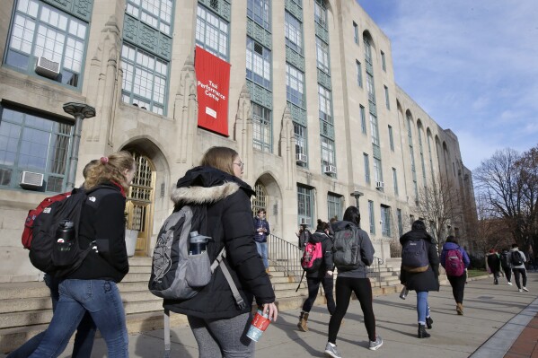 FILE - Students and passers-by walk past an entrance to Boston University College of Arts and Sciences, Nov. 29, 2018, in Boston. As more than 2 million graduating high school students from across the United States finalize their decisions on what college to attend this fall, many are facing jaw-dropping costs — in some cases, as much as $95,000. (AP Photo/Steven Senne, File)