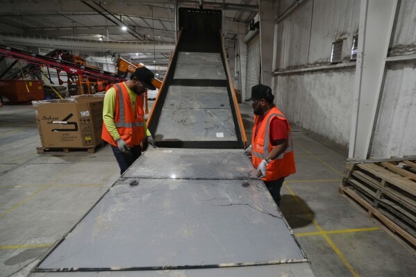 Workers feed solar panels onto a conveyer belt as the panels are processed at We Recycle Solar on Tuesday, June 6, 2023, in Yuma, Ariz. (AP Photo/Gregory Bull)