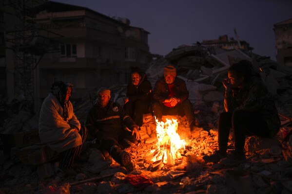A family keeps warm by a fire as they follow a rescue team searching for relatives in earthquake-destroyed buildings in Antakya, southern Turkey, Feb. 15, 2023. (AP Photo/Francisco Seco)