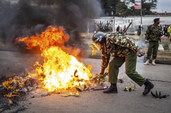 A police officer tries to put out a burning barricade erected by demonstrators during protests in the capital Nairobi, Kenya Friday, July 7, 2023. Dozens of anti-government protesters were arrested in Nairobi on Friday as other parts of the country also witnessed demonstrations called by the opposition against newly imposed taxes and the cost of living. (AP Photo/Samson Otieno)