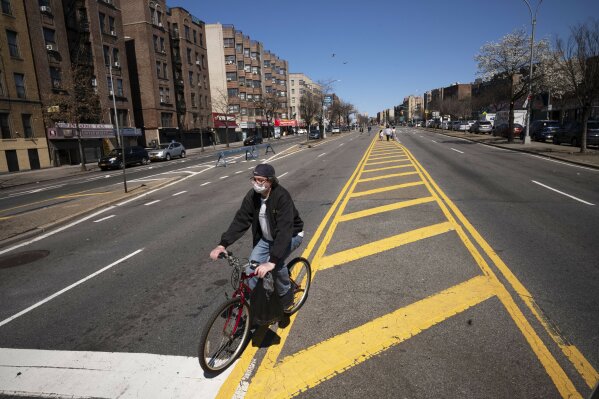 A man wearing a mask bicycles along a section of the Grand Concourse that has been temporarily closed to vehicular traffic as the city tests out a pilot program providing more social distancing space during the coronavirus pandemic, Friday, March 27, 2020 in the Bronx borough of New York. (AP Photo/Mark Lennihan)
