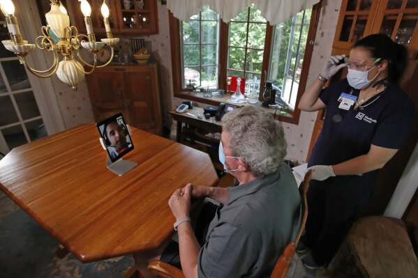Nurse practitioner Sadie Paez, far right, watches a telehealth session with patient William Merry, who is recovering from pneumonia at his home, Thursday, July 9, 2020, in Ipswich, Mass. As hospitals care for people with COVID-19 and try to keep others from catching the virus, more patients are opting to be treated where they feel safest: at home. (AP Photo/Elise Amendola)