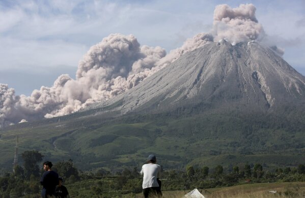 People watch as Mount Sinabung spews volcanic materials during an eruption in Karo, North Sumatra, Indonesia, Thursday, March 11, 2021. The volcano unleashed an avalanche of searing gas clouds flowing down its slopes during eruption on Thursday. No casualties were reported. (AP Photo/Binsar Bakkara)