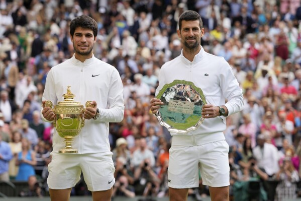 Spain's Carlos Alcaraz, left, celebrates with the trophy after beating Serbia's Novak Djokovic, right, to win the final of the men's singles on day fourteen of the Wimbledon tennis championships in London, Sunday, July 16, 2023. (AP Photo/Kirsty Wigglesworth)