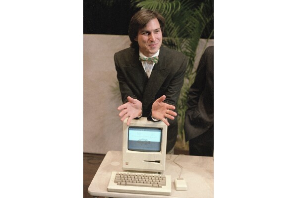 FILE - Steven Jobs, then chairman of the board of Apple Computer, leans on the new Macintosh personal computer following a shareholder's meeting Jan. 24, 1984, in Cupertino, Ca. The Macintosh computer lived up to the revolutionary promise made by Apple co-founder Jobs at it's 1984 unveiling. (APPhoto/Paul Sakuma, File)