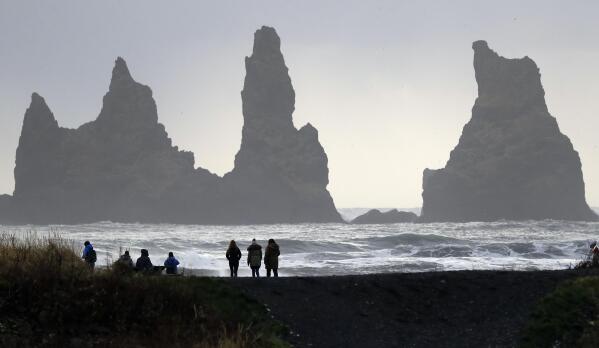 FILE - In this Oct. 26, 2016 file photo, people walk on the black sanded beach in Vik, Iceland, near the Volcano Katla. After a summer of increased seismic activity at Katla, Icelanders are obsessing over the smallest sign of an eruption at the country’s most closely watched volcano. Katla last erupted in 1918. Never before in recorded history, dating back to the 12th century, have 99 years passed without an eruption from the volcano. (AP Photo/Frank Augstein, File)
