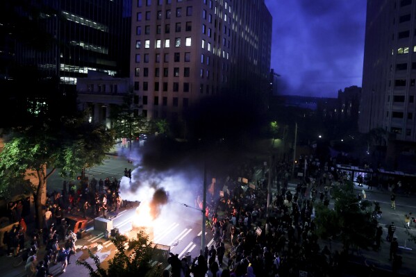 Protestors surround a dumpster that was set on fire in front of the Henry M. Jackson Federal Building during a protest against federal immigration arrests, Wednesday, June 11, 2025, in Seattle. (AP Photo/Ryan Sun)