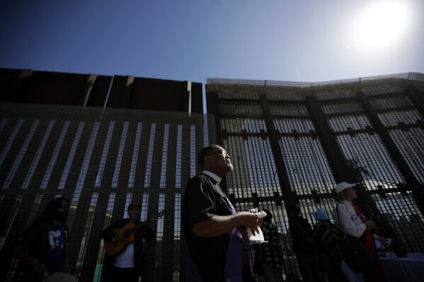 
              In this April 3, 2017 photo, Reverend Guy A. Leemhuis, center, of the Holy Faith Episcopal Church of Los Angeles, leads a song on the U.S. side of the border fence separating Tijuana, Mexico, from San Diego. With bids due Tuesday, April 4, 2017, on the first design contracts, companies are preparing for the worst if they get the potentially lucrative but controversial job. Groups are already planning protests and prayer vigils for both sides of the border. (AP Photo/Gregory Bull)
            