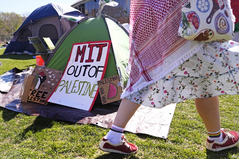 A woman walks past a sign where students protest at an encampment on the campus of the Massachusetts Institute of Technology.