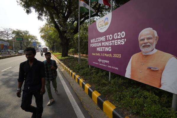 Commuters walk past a banner with Indian Prime Minister's Narendra Modi photograph welcoming delegates of G20 foreign ministers meeting, in New Delhi, India, Wednesday, March 1, 2023. Fractured East-West relations over Russia's war in Ukraine and increasing concerns about China's global aspirations are set to dominate what is expected to be a highly contentious meeting of foreign ministers from the world's largest industrialized and developing nations this week in India. (AP Photo/Manish Swarup)