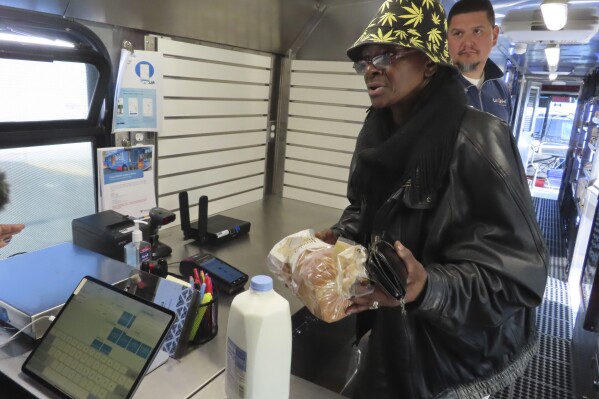 Delorese Butley-Whaley brings her purchases of milk and bread to the register of a specially modified bus that serves as a mobile supermarket in Atlantic City N.J. on Friday, Dec. 8, 2023. Virtua Health and the New Jersey Economic Development Authority are operating a service to bring fresh groceries and produce to Atlantic City, where plans for what would be the city's first supermarket in nearly 20 years recently fell through. (AP Photo/Wayne Parry)