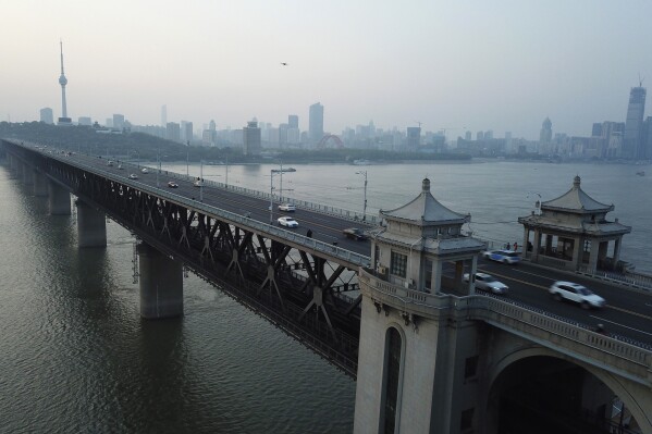 The sun sets behind the Wuhan Yangtze River Bridge and the Tortoise Mountain TV Tower in Wuhan in central China's Hubei province on April 12, 2020. (AP Photo/Sam McNeil, File)