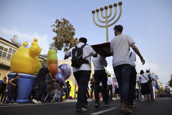 FILE - In this Oct. 17, 2019 file photo, people carry a Menorah as they participate in the annual support march for Israel, during the Jewish holiday of Sukkot, in Jerusalem. An evangelical broadcaster who boasted of miraculously securing a TV license in Israel now risks being taken off the air over suspicions of trying to convert Jews to Christianity. The controversy over “GOD TV” has put both Israel and its evangelical Christian allies in an awkward position. Evangelical Christians, particularly in the United States, are among Israel's strongest supporters. Israel has long welcomed their political and financial support, especially as their influence has risen during the Trump era. (AP Photo/Oded Balilty, File )